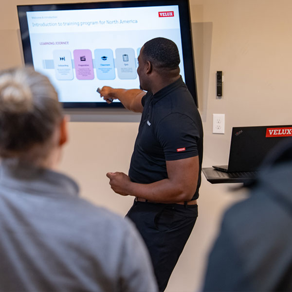 A presenter points to a "Learning Journey" diagram on a large monitor during a VELUX training session.